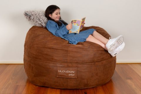 Girl relaxing and reading on an Urban KloudSac with a shaggy brown fur cushion for her head.