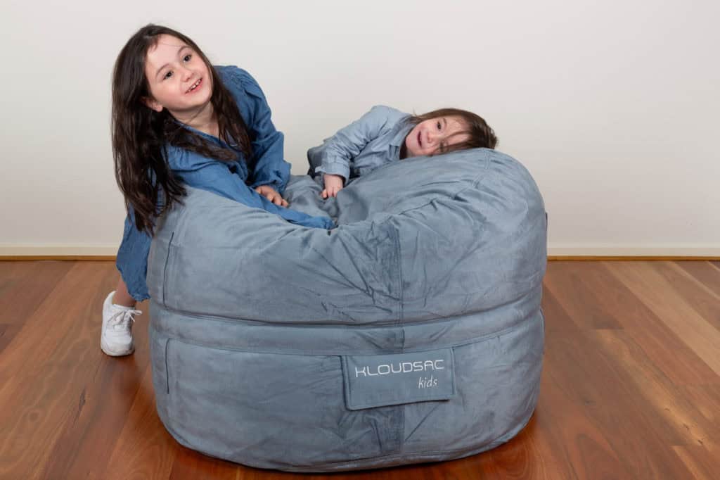 Young brother and sister are playing on a Kids KloudSac Foam Filled Bean Bag inside.