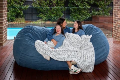 A young family are sitting on together on a large KloudSac Lounge outside next to the pool, laughing together while cuddling under a stone fur calming blanket.