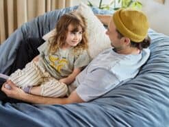 Child and father sitting together on a foam filled bean bag in a peaceful living room.