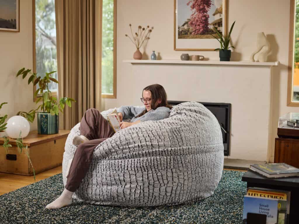 A teenage girl relaxing on a large foam filled Mondo Stone Fur bean bag in a well-decorated living room.