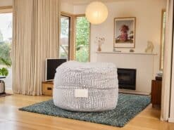 Comfortable foam filled Mondo bean bag placed on a rug in a bright living room with large windows and modern decor.