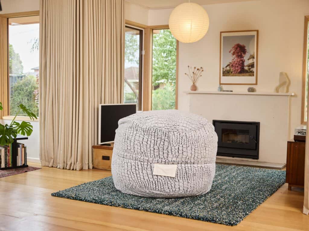 Plush Stone Faux Fur foam filled Urban bean bag in a peaceful living room setting with large windows and modern decor.